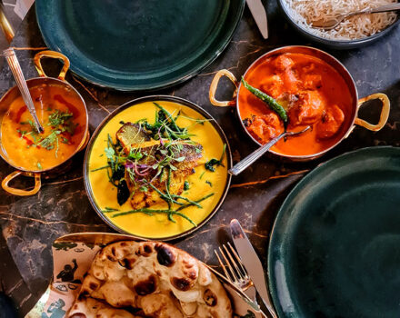 copper dishes of curry with bowls of rice and bread on a table