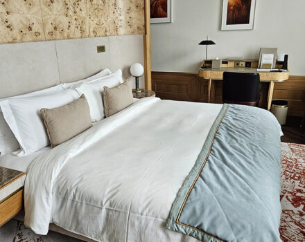 hotel room with a king-size bed, decorative headboard, writing desk and patterned rug